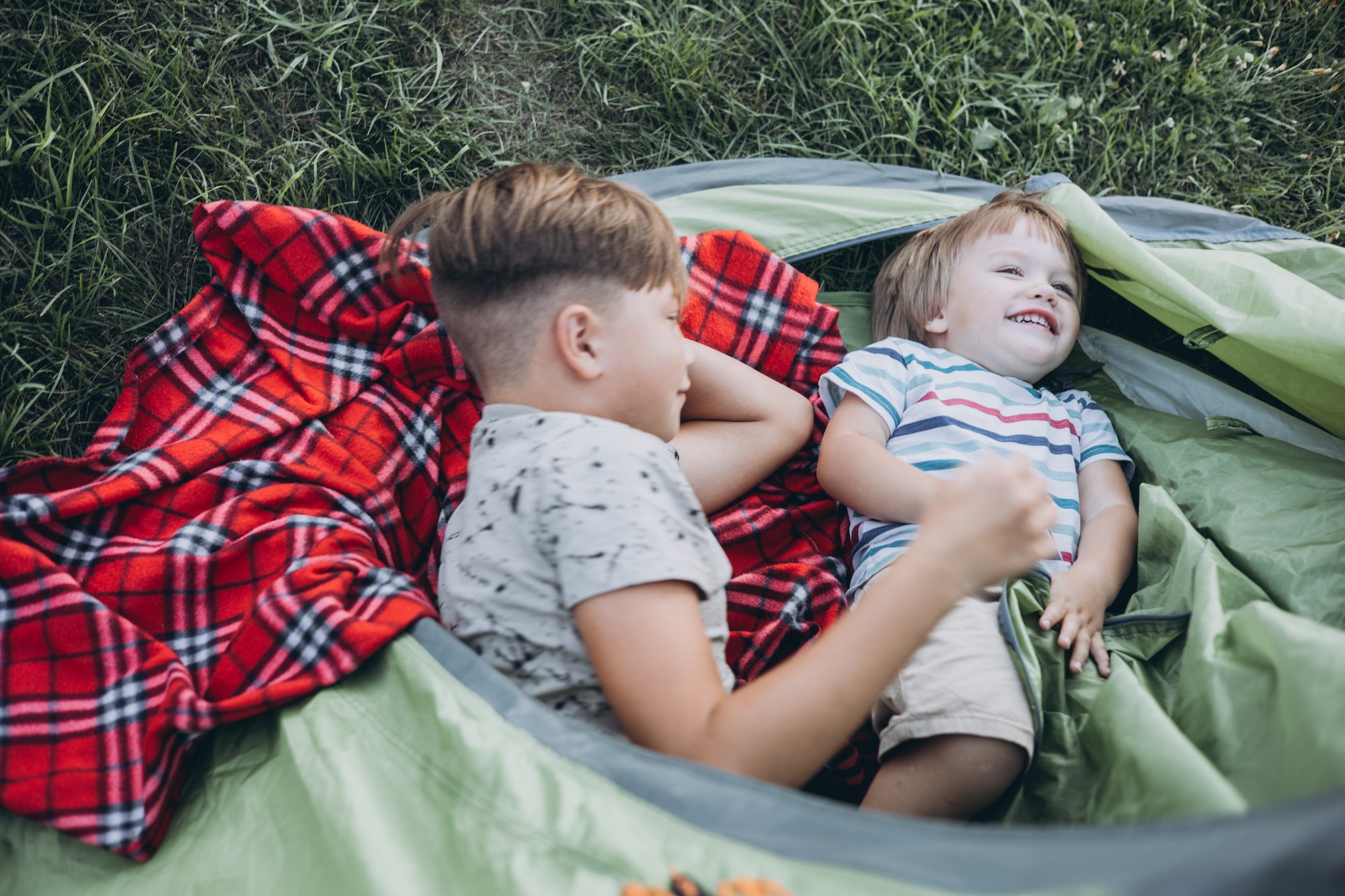 Children lying with plaid in camping tent. Family weekend nature outdoor.