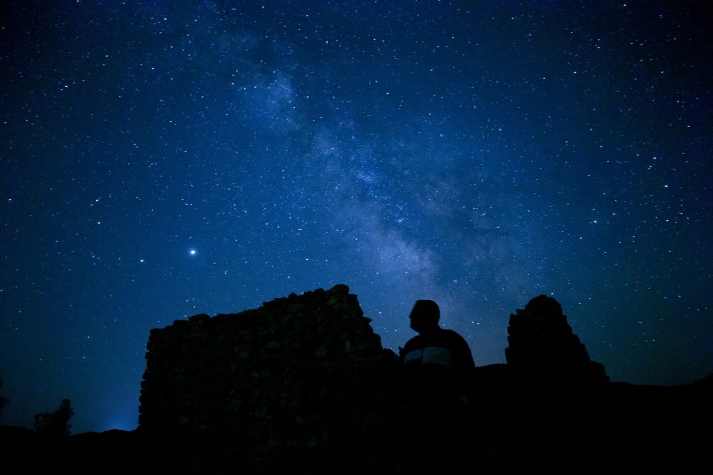 Magical view of silhouettes of a man sitting on the cliff stargazing the starry night sky