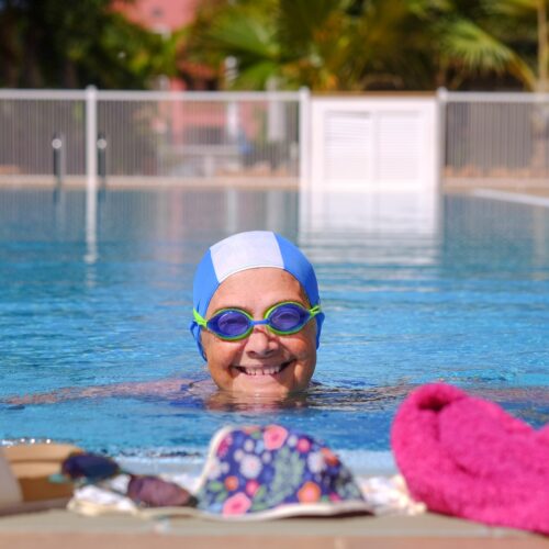 Smiling senior woman swimming into the outdoor swimming pool wearing swimming goggles
